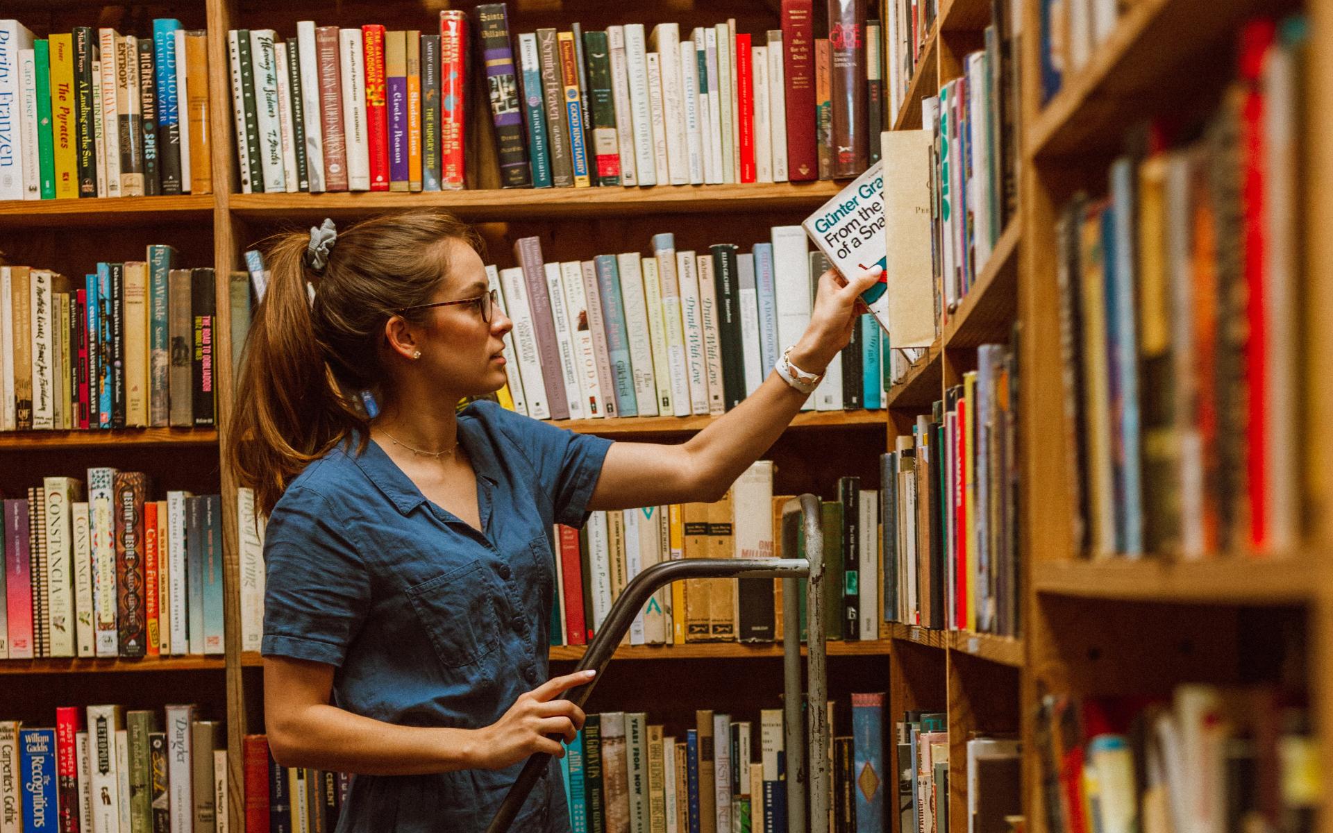 Junge Frau auf einer Leiter vor dem Bücherregal